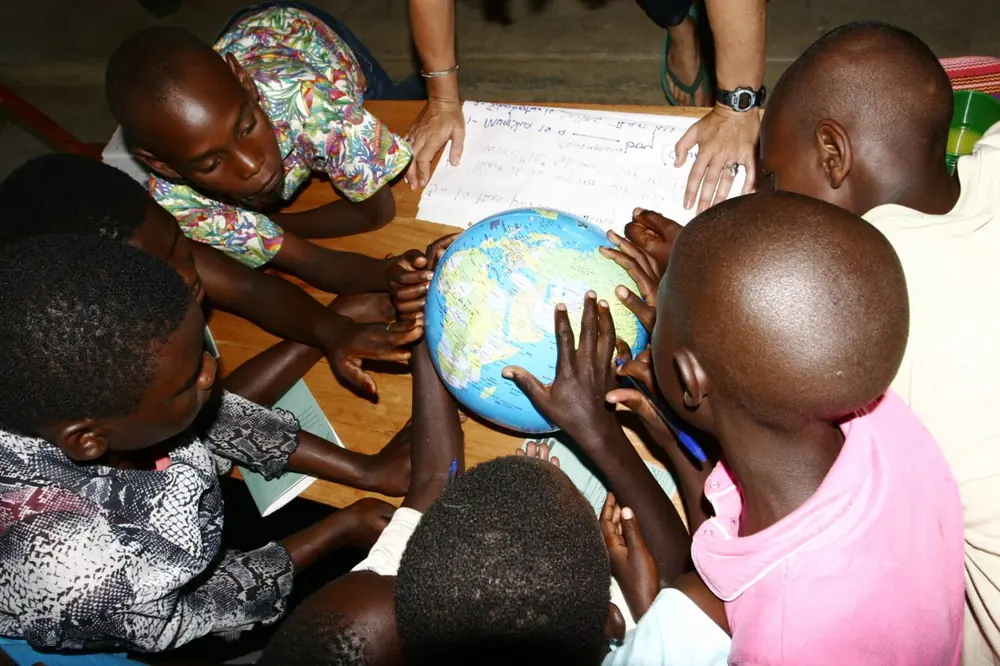 Students crowd around an inflatable globe during a lesson, pointing at places on the map