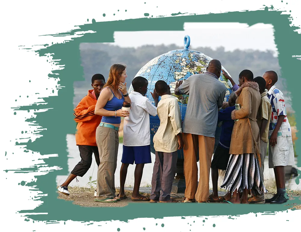 A volunteer and students from Uganda gathered around a large blue globe beside a lake
