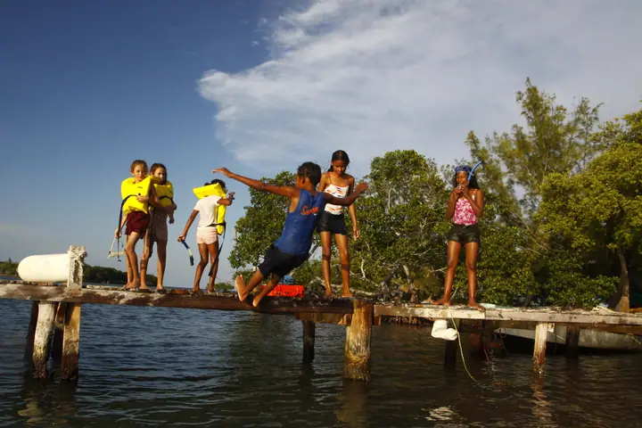 Young Belizean kids having fun jumping off a dock into the Caribbean Sea.