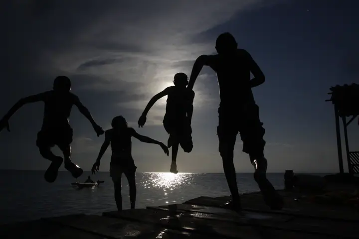 Young Belizean kids having fun jumping off a dock into the Caribbean Sea.