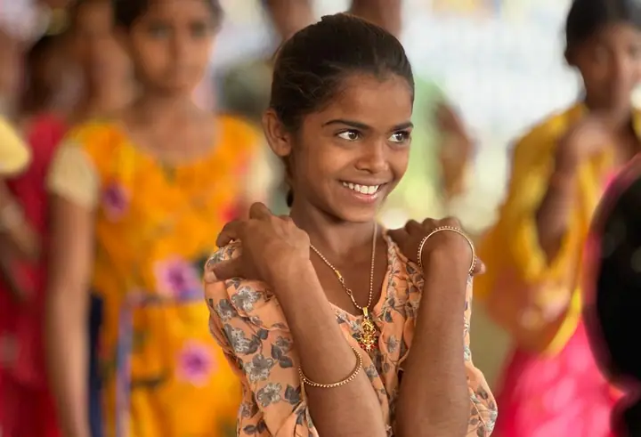 A smiling girl in a floral top with other students blurred behind her
