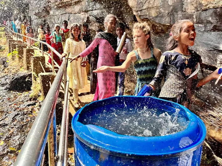 Students and volunteers gathered at a railing beside a blue water tank